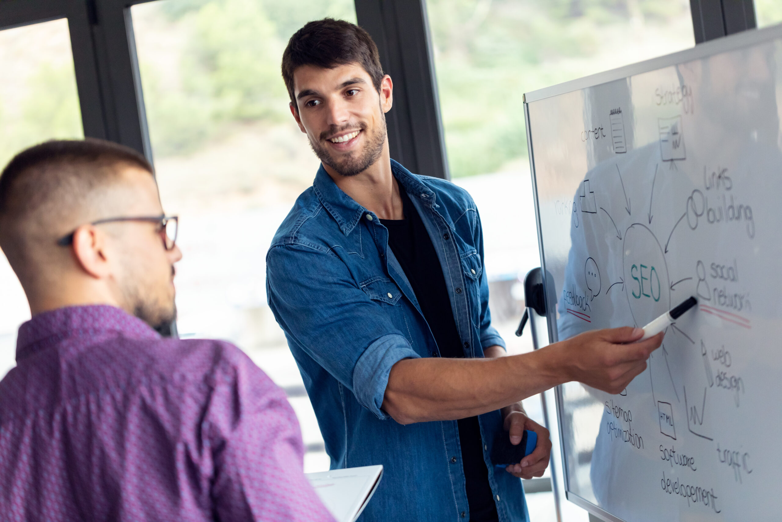 SEO Agentur Blitz Berlin – Mitarbeiter erklärt Kollegen Strategie auf der Über uns-Seite